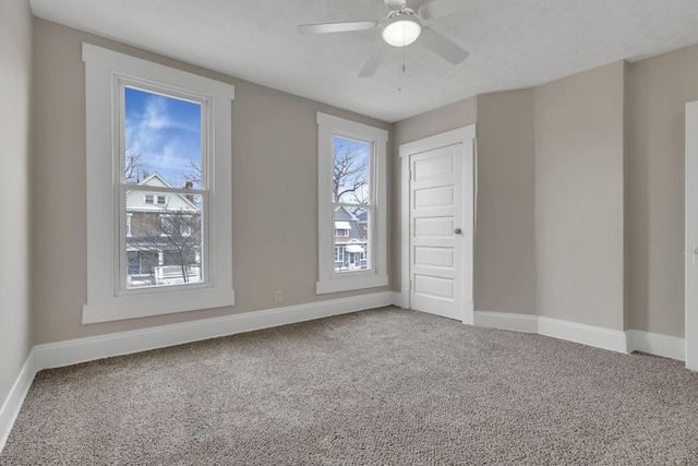 carpeted empty room featuring a ceiling fan, a textured ceiling, and baseboards