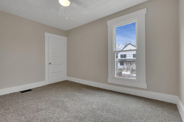 empty room featuring carpet floors, visible vents, a textured ceiling, and baseboards