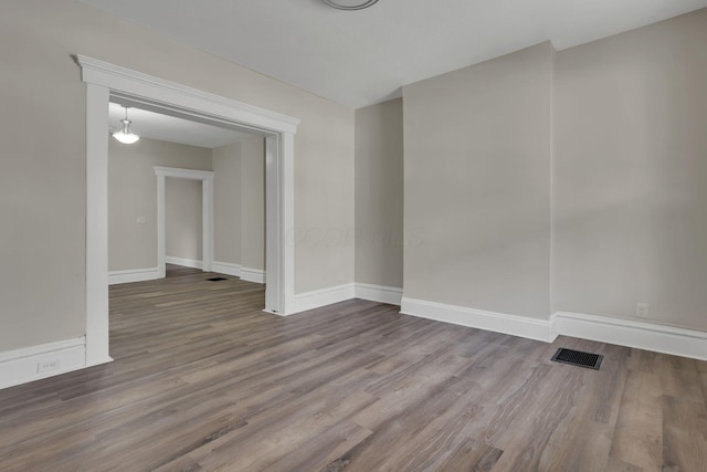 empty room with wood finished floors, visible vents, and baseboards