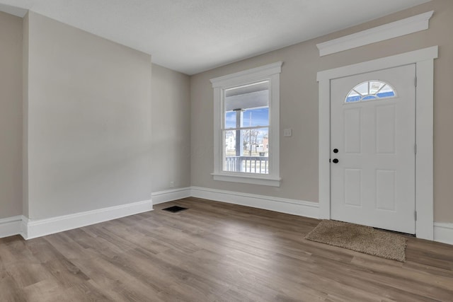 entryway with visible vents, a textured ceiling, baseboards, and wood finished floors