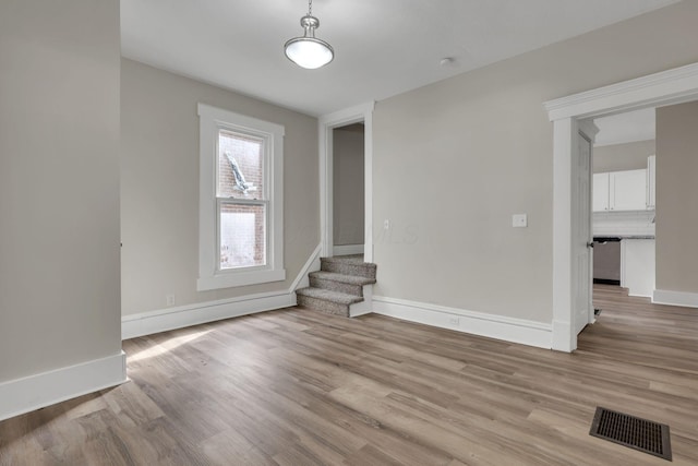 unfurnished room featuring light wood-style floors, visible vents, stairway, and baseboards