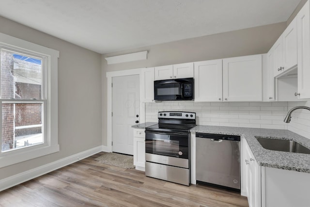 kitchen featuring light stone counters, stainless steel appliances, decorative backsplash, a sink, and light wood-type flooring