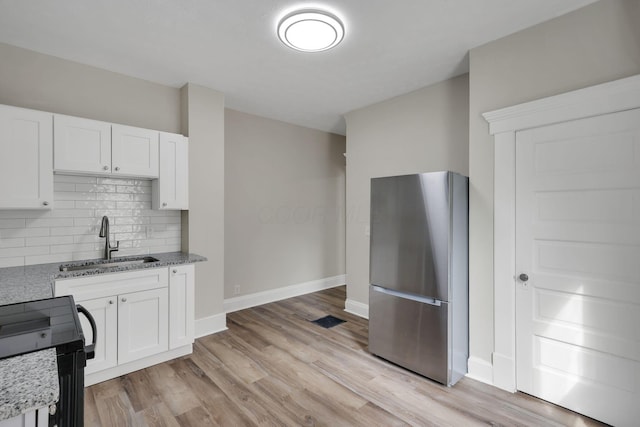 kitchen with a sink, white cabinetry, freestanding refrigerator, light stone countertops, and tasteful backsplash