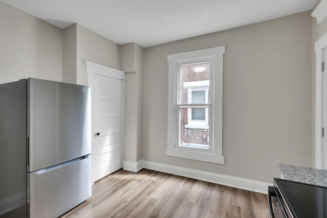 kitchen featuring freestanding refrigerator, light wood-style flooring, baseboards, and light stone countertops