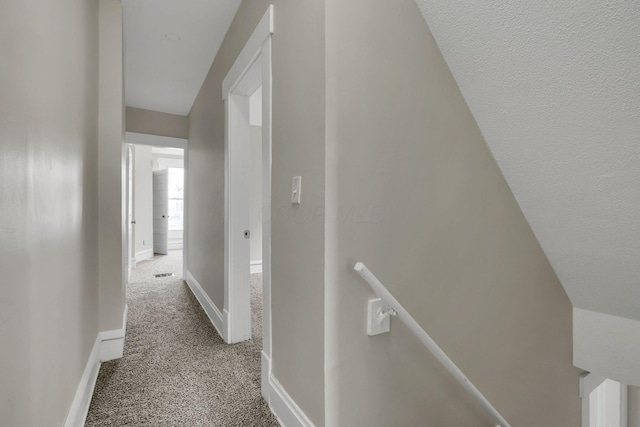 hall with carpet, baseboards, and an upstairs landing