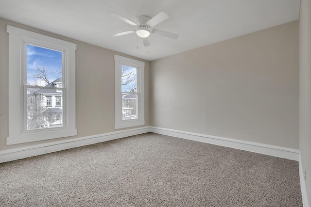 carpeted spare room with a ceiling fan and baseboards