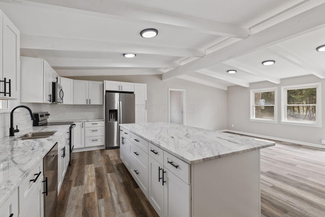 kitchen featuring lofted ceiling with beams, a sink, a center island, appliances with stainless steel finishes, and decorative backsplash