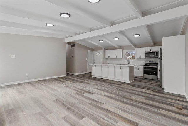 kitchen featuring vaulted ceiling with beams, stainless steel appliances, light countertops, open floor plan, and white cabinets