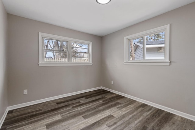 empty room featuring baseboards, dark wood-type flooring, and a healthy amount of sunlight