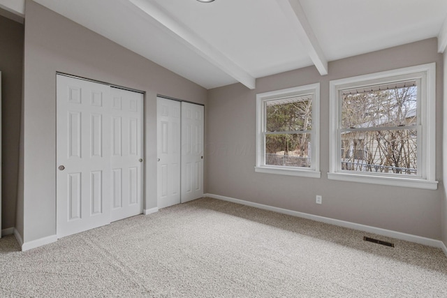 unfurnished bedroom with baseboards, visible vents, lofted ceiling with beams, carpet flooring, and two closets