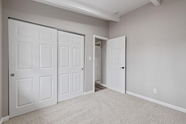 unfurnished bedroom featuring carpet floors, a closet, baseboards, and beam ceiling