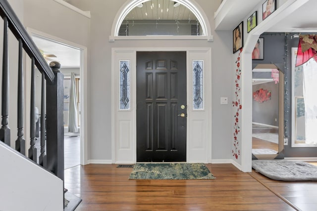 foyer entrance with stairway, wood-type flooring, a high ceiling, and baseboards