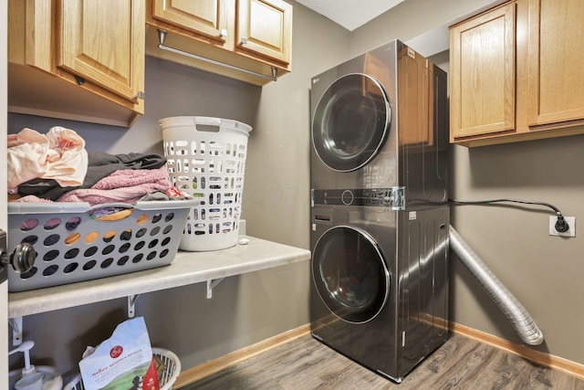 washroom featuring baseboards, cabinet space, stacked washing maching and dryer, and wood finished floors