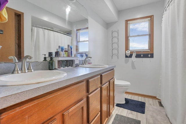 full bath featuring baseboards, a sink, toilet, and double vanity