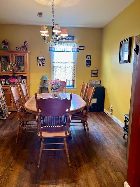 dining space featuring a notable chandelier, visible vents, baseboards, and dark wood-type flooring