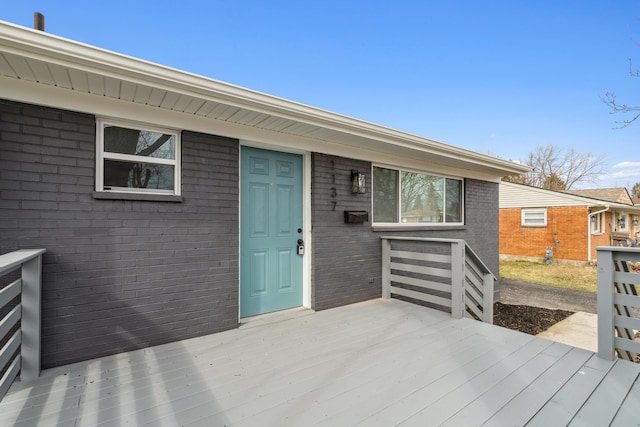 view of exterior entry featuring brick siding and a wooden deck