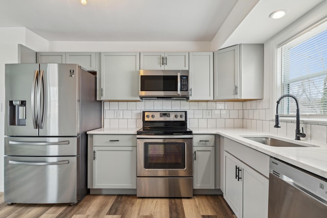 kitchen with appliances with stainless steel finishes, gray cabinets, a sink, and light countertops