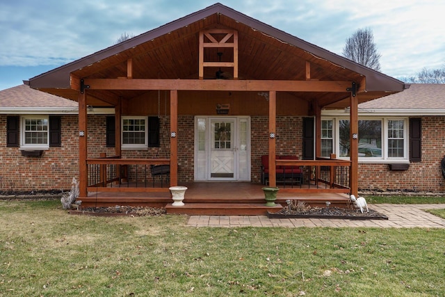 view of front of property with covered porch, a front lawn, roof with shingles, and brick siding