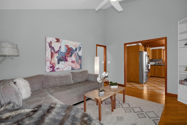 living area with light wood-type flooring, a high ceiling, ceiling fan, and baseboards