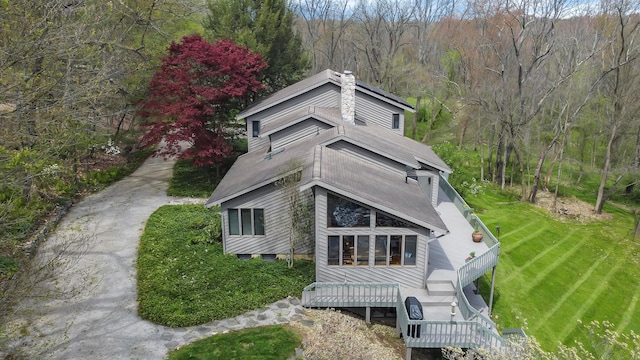 rear view of property featuring a forest view, a lawn, and a wooden deck