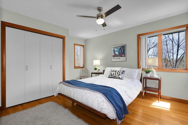 bedroom with light wood finished floors, a ceiling fan, baseboards, and a closet