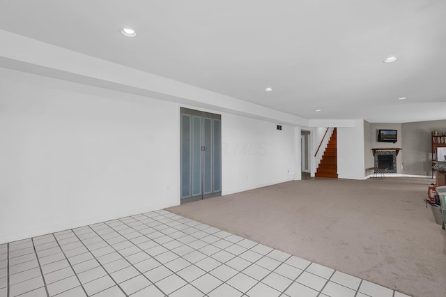 unfurnished living room with stairs, a fireplace with raised hearth, carpet flooring, and recessed lighting