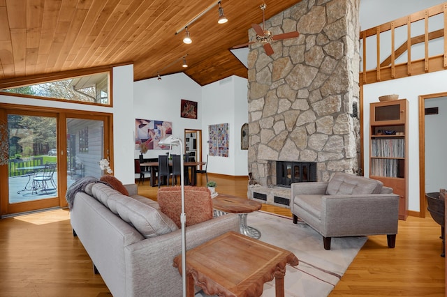 living room with high vaulted ceiling, a stone fireplace, wood ceiling, light wood-type flooring, and rail lighting