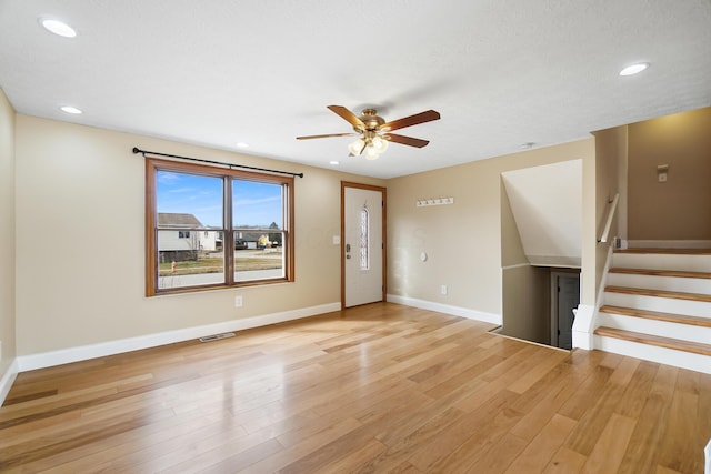 interior space with light wood-type flooring, visible vents, a ceiling fan, stairway, and baseboards