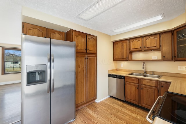 kitchen with light wood-style flooring, a sink, stainless steel appliances, brown cabinetry, and light countertops