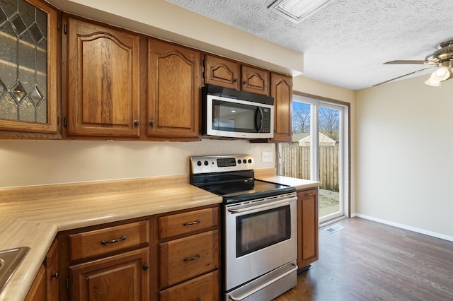 kitchen with dark wood finished floors, light countertops, brown cabinets, stainless steel appliances, and a textured ceiling