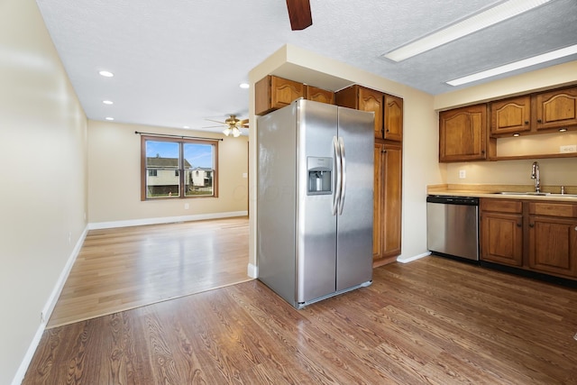 kitchen with dark wood-type flooring, brown cabinetry, appliances with stainless steel finishes, and a sink