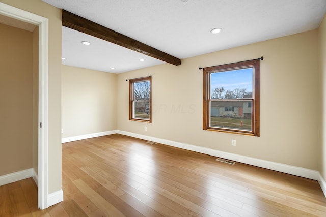 empty room with visible vents, beamed ceiling, a healthy amount of sunlight, and wood finished floors