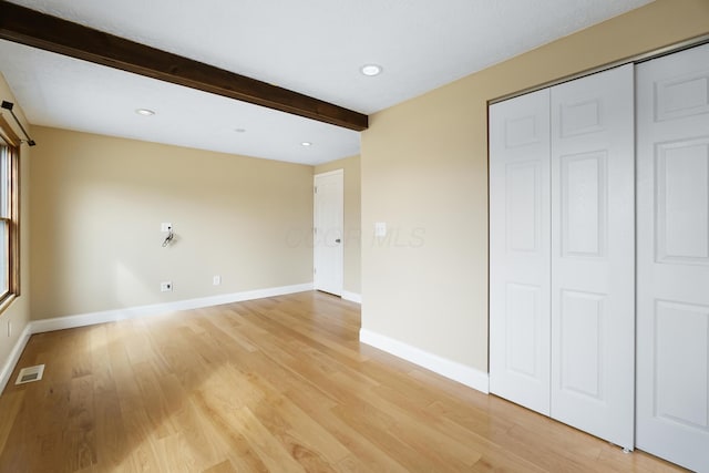 interior space with light wood-style floors, baseboards, visible vents, and beam ceiling