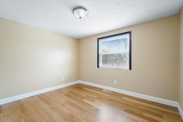 spare room with a textured ceiling, light wood-style floors, visible vents, and baseboards