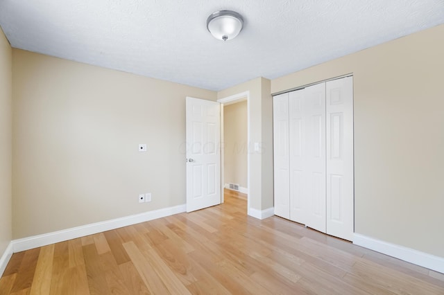 unfurnished bedroom with light wood-style flooring, baseboards, a closet, and a textured ceiling