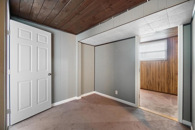 unfurnished bedroom with a closet, carpet floors, wooden walls, wooden ceiling, and baseboards