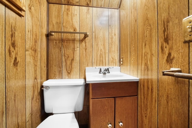 bathroom with vanity, wooden walls, and toilet