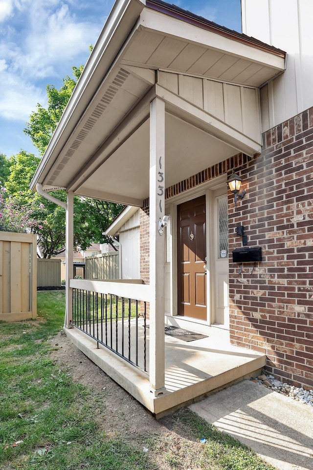 property entrance with brick siding, board and batten siding, fence, and a lawn