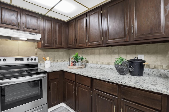 kitchen with electric stove, tasteful backsplash, dark brown cabinets, and under cabinet range hood