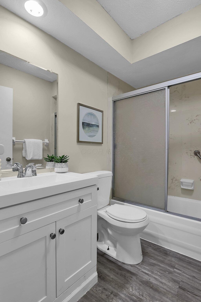 full bathroom with a textured ceiling, toilet, wood finished floors, vanity, and combined bath / shower with glass door