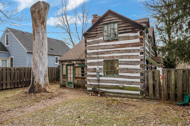 rear view of property with log siding, fence, roof with shingles, and a chimney