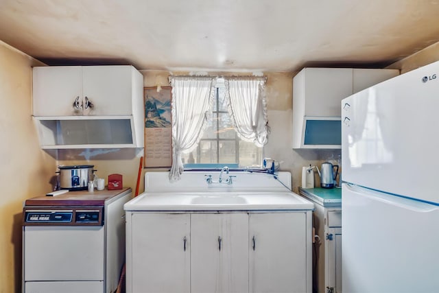 kitchen featuring a sink, white cabinetry, freestanding refrigerator, and light countertops