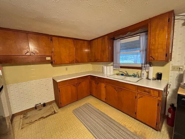 kitchen with a textured ceiling, a sink, light countertops, light floors, and brown cabinetry