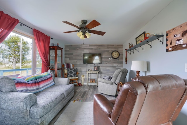 living room featuring an accent wall, a ceiling fan, wooden walls, and wood finished floors