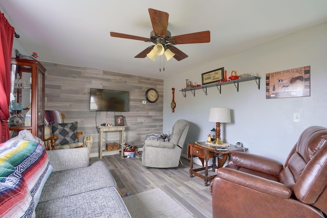 living room featuring wooden walls, an accent wall, a ceiling fan, and wood finished floors