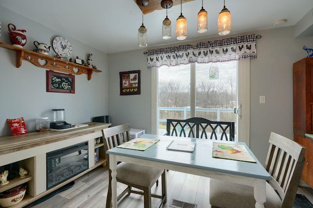 dining room with light wood-style floors, a glass covered fireplace, and visible vents