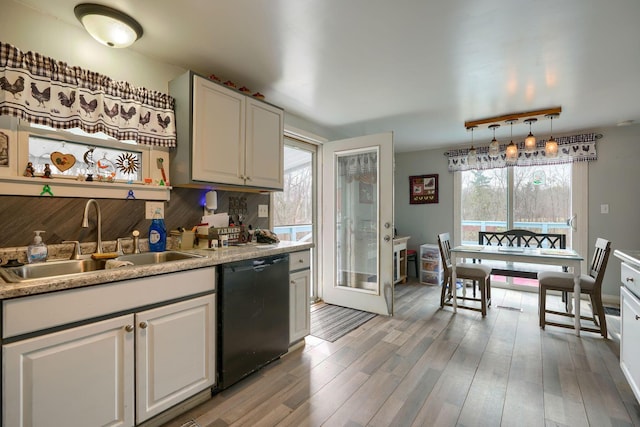 kitchen with black dishwasher, light countertops, decorative backsplash, a sink, and light wood-type flooring