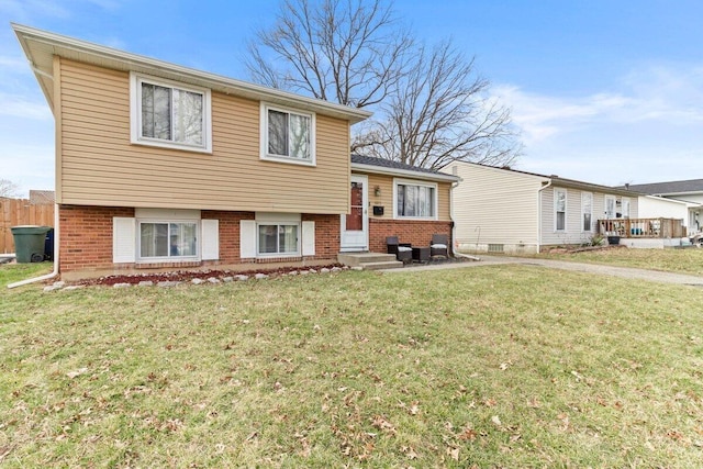 tri-level home featuring entry steps, brick siding, and a front lawn