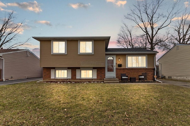 split level home featuring entry steps, a front yard, and brick siding