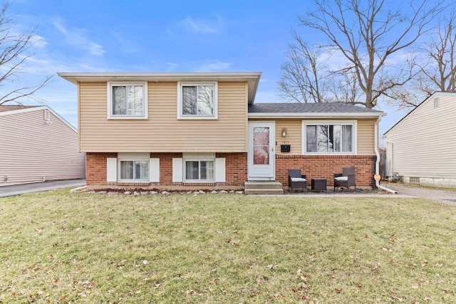 tri-level home featuring entry steps, brick siding, and a front yard